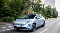 Hellblauer MG4 EV Urban Luxury während der Fahrt auf einer mehrspurigen Straße in städtischer Umgebung.