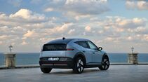 Hyundai Ioniq 3 in Ice Blue Pearl aus der Heck-Dreiviertelansicht auf einer Terrasse mit Meer und Wolkenhimmel im Hintergrund.