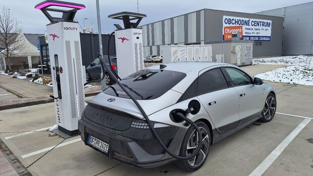 Hyundai Ioniq 6 an Ionity-Ladesaeule, Ladekabel angeschlossen, Heck-Seitenansicht, Parkplatz im Winter.