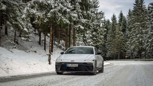 Hyundai Ioniq 6 frontal auf verschneiter Landstraße im Wald, Winterwetter, Fahrbahn mit Schneeresten.