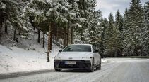 Hyundai Ioniq 6 frontal auf verschneiter Landstraße im Wald, Winterwetter, Fahrbahn mit Schneeresten.