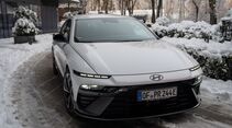Hyundai Ioniq 6 parkend im Schnee vor einem Gebäude, Frontansicht schräg, verschneite Umgebung.