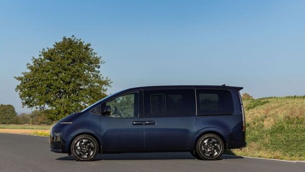 Hyundai Staria Elektro in Dunkelblau von der Seite mit langer Karosserie, großen Seitenfenstern, Schiebetür und schwarzen Rädern.
