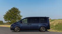 Hyundai Staria Elektro in Dunkelblau von der Seite mit langer Karosserie, großen Seitenfenstern, Schiebetür und schwarzen Rädern.