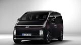 Hyundai Staria Elektro in dunkler Lackierung aus schräger Frontansicht mit durchgehendem Lichtband und vertikalen Scheinwerfern.