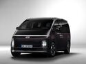 Hyundai Staria Elektro in dunkler Lackierung aus schräger Frontansicht mit durchgehendem Lichtband und vertikalen Scheinwerfern.