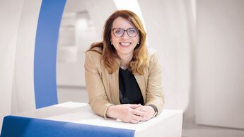 Imelda Labbé, Präsidentin des VDIK, lächelt in die Kamera und lehnt auf einem weißen Podest in einem modernen Innenraum.