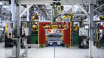 Industrieroboter arbeiten in einer Automobilfabrik an einer automatisierten Fertigungslinie mit Schutzvorhängen und Anlagensteuerung.