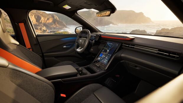 Innenraum des Ford Explorer mit großem vertikalem Touchscreen, Cockpit und Blick auf eine Küstenlandschaft durch die Frontscheibe.
