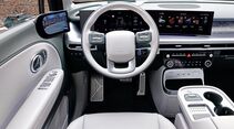 Innenraum des Hyundai Ioniq 9 mit Lenkrad, digitalem Kombiinstrument, breitem Zentraldisplay und Mittelkonsole aus Fahrersicht.