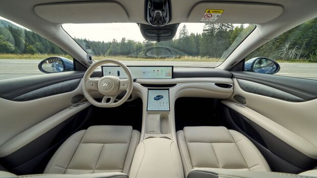 Innenraum des MG IM5 mit Lenkrad, breitem Display im Armaturenbrett, zentralem Touchscreen und hellen Vordersitzen.