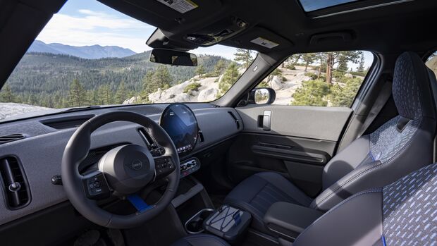 Innenraum des MINI Countryman Untamed Edition mit gemusterten Vordersitzen, rundem Zentraldisplay, blauen Details und Glasdach.