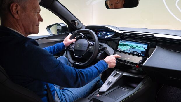 Innenraum des Peugeot E-408 Facelift mit Fahrer am Lenkrad und Infotainment-Display in der Mittelkonsole