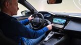 Innenraum des Peugeot E-408 Facelift mit Fahrer am Lenkrad und Infotainment-Display in der Mittelkonsole