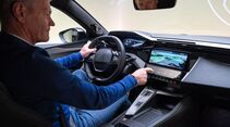 Innenraum des Peugeot E-408 Facelift mit Fahrer am Lenkrad und Infotainment-Display in der Mittelkonsole