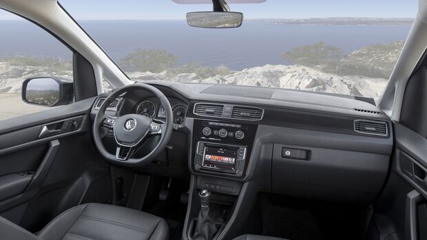 Innenraum eines VW Caddy mit Lenkrad, Armaturenbrett und Infotainment-System, Blick durch die Frontscheibe auf eine Küstenlandschaft
