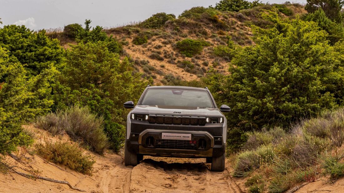 Jeep Compass 4xe auf einer sandigen Offroad-Strecke zwischen Dünen und Sträuchern in Frontansicht.