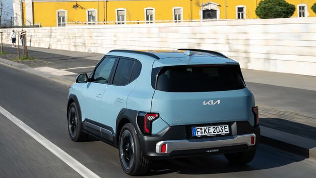 Kia EV2 in Frost Blue während der Fahrt, aufgenommen schräg von hinten mit Blick auf Heck und linke Fahrzeugseite.