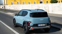 Kia EV2 in Frost Blue während der Fahrt, aufgenommen schräg von hinten mit Blick auf Heck und linke Fahrzeugseite.