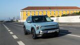 Kia EV2 in Frost Blue während der Fahrt, aufgenommen schräg von vorn auf einer Stadtstraße.