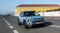 Kia EV2 in Frost Blue während der Fahrt, aufgenommen schräg von vorn auf einer Stadtstraße.