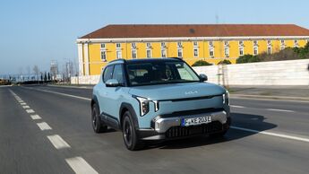 Kia EV2 in Frost Blue während der Fahrt, aufgenommen schräg von vorn auf einer Stadtstraße.