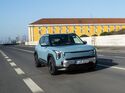 Kia EV2 in Frost Blue während der Fahrt, aufgenommen schräg von vorn auf einer Stadtstraße.