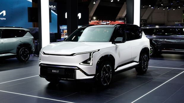 Kia EV5 GT in Weiß mit schwarzem Dach als Front-Seitenansicht auf einer Automesse mit Beleuchtung und Messestand.