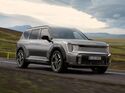 Kia EV9 GT als graues Elektro-SUV bei der Fahrt auf einer Landstrasse vor einer weitlaeufigen Berglandschaft.