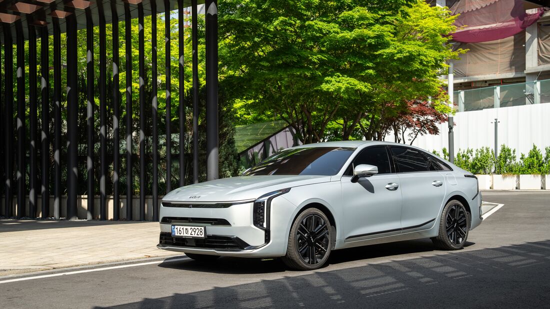 Kia K8 in Front- und Seitenansicht vor modernem Gebäude mit Grünanlagen.