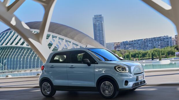 Kompakter Elektro-Kleinwagen Leapmotor T03 fährt in urbaner Umgebung an moderner Architektur vorbei.