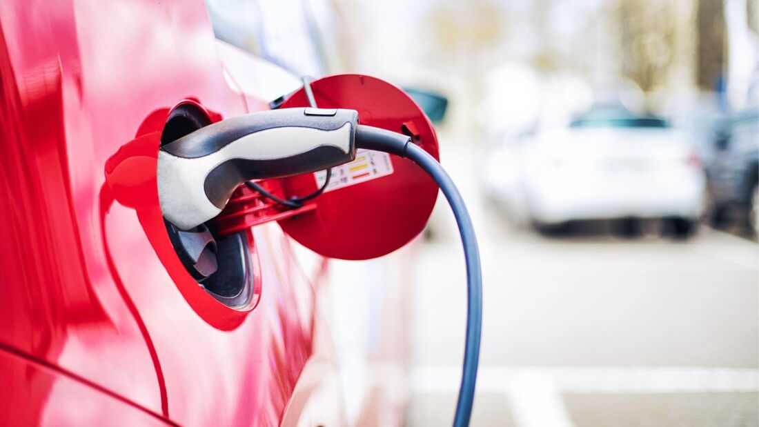 Ladekabel steckt in der Ladebuchse eines roten Elektroautos auf einem Parkplatz.