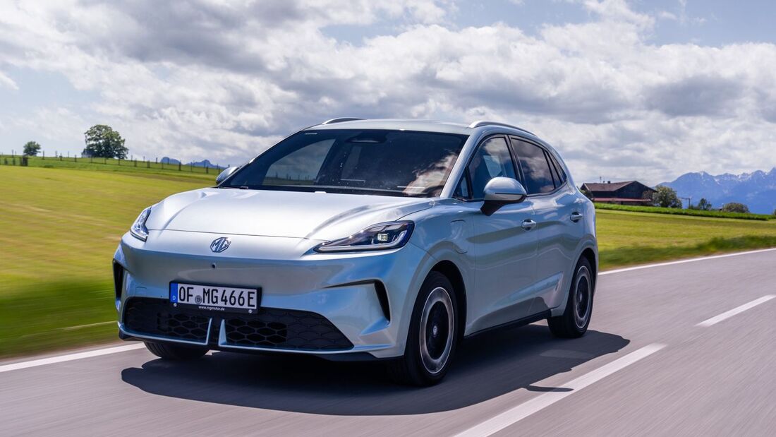 MG4 EV Urban Luxury in Hellblau bei der Fahrt auf einer Landstraße vor Wiesen und Berglandschaft.