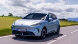 MG4 EV Urban Luxury in Hellblau bei der Fahrt auf einer Landstraße vor Wiesen und Berglandschaft.