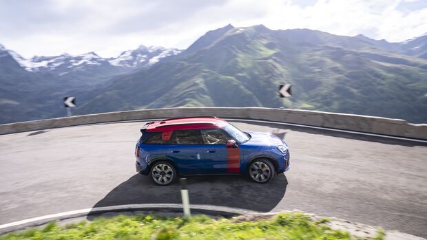 MINI Countryman JCW auf einer Passstraße in einer engen Kurve vor alpiner Bergkulisse.