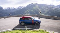 MINI Countryman JCW auf einer Passstraße in einer engen Kurve vor alpiner Bergkulisse.