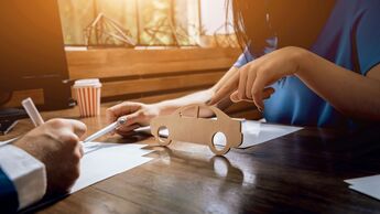 Man signing a car insurance policy, the agent is holding the wooden car model.