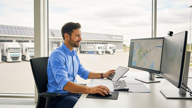 Mann arbeitet an Computer mit Fuhrparksoftware vor Logistikstandort mit Fahrzeugen