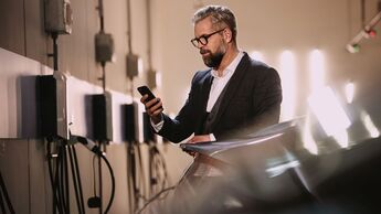 Mann bedient mit einem Smartphone den Ladevorgang eines Elektroautos an einer Wallbox in einer Tiefgarage