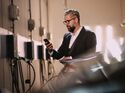 Mann bedient mit einem Smartphone den Ladevorgang eines Elektroautos an einer Wallbox in einer Tiefgarage