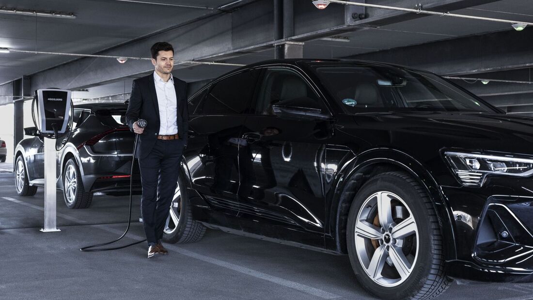 Mann mit Dienstwagen beim Laden eines Elektroautos an einer Ladestation in einem Parkhaus