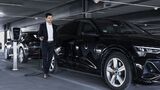 Mann mit Dienstwagen beim Laden eines Elektroautos an einer Ladestation in einem Parkhaus