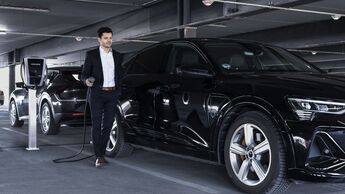 Mann mit Dienstwagen beim Laden eines Elektroautos an einer Ladestation in einem Parkhaus