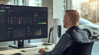 Mann sitzt an einem Arbeitsplatz und analysiert Fuhrparkdaten auf einem Bildschirm, im Hintergrund ein Elektroauto an einer Ladestation