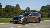 Mazda CX-80 in Melting Copper in Seitenansicht während der Fahrt auf einer Landstraße.