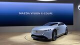 Mazda Vision X-Coupé auf einer Präsentationsbühne vor einer Leinwand mit der Aufschrift „MAZDA VISION X-COUPE“.