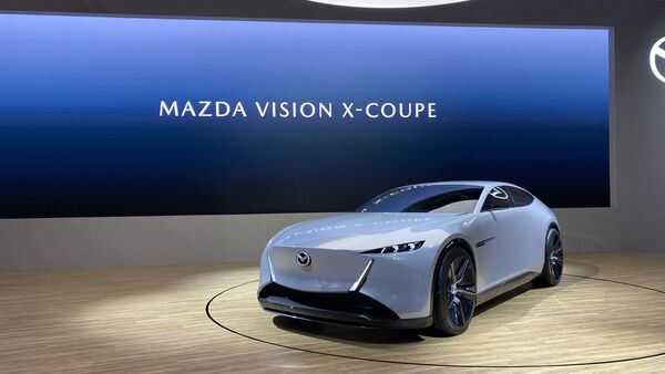 Mazda Vision X-Coupé auf einer Präsentationsbühne vor einer Leinwand mit der Aufschrift „MAZDA VISION X-COUPE“.