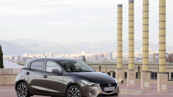 Mazda2 Typ DJ aus schraeg vorn im weiten Bildausschnitt, Fahrzeug steht im Freien.