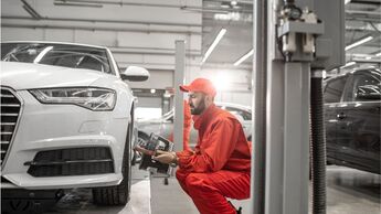 Mechaniker prüft in einer Werkstatt die Front eines Pkw auf einer Hebebühne bei einer Unfallreparatur.