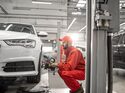 Mechaniker prüft in einer Werkstatt die Front eines Pkw auf einer Hebebühne bei einer Unfallreparatur.